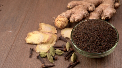 Black Tea Powder or dry dust tea powder, chai patti isolated in wooden bowl with Cardamom, Clove and Ginger.