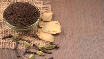 Black Tea Powder or dry dust tea powder, chai patti isolated in wooden bowl with Cardamom, Clove and Ginger.