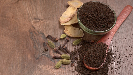 Black Tea Powder or dry dust tea powder, chai patti isolated in wooden bowl with Cardamom, Clove...