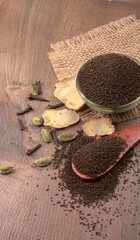 Black Tea Powder or dry dust tea powder, chai patti isolated in wooden bowl with Cardamom, Clove and Ginger.