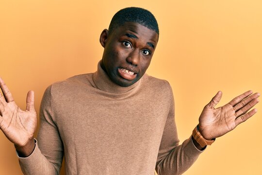 Young african american man wearing casual winter sweater clueless and confused with open arms, no idea and doubtful face.