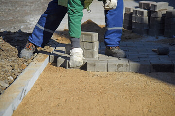 A worker in overalls lays out paving slabs on the sand in even rows,building a road for pedestrians.