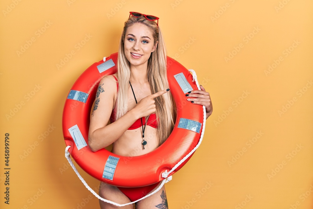 Sticker young caucasian woman wearing bikini and holding lifeguard float cheerful with a smile on face point