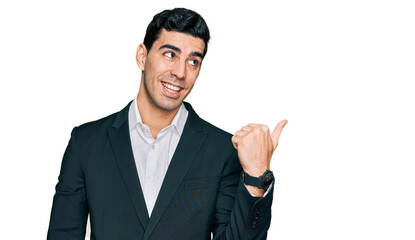Handsome hispanic man wearing business clothes smiling with happy face looking and pointing to the side with thumb up.