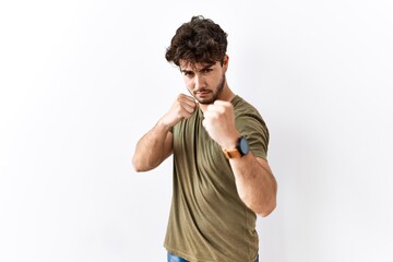 Hispanic man standing over isolated white background ready to fight with fist defense gesture, angry and upset face, afraid of problem