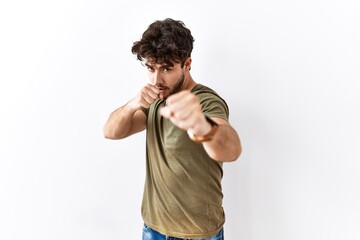 Hispanic man standing over isolated white background punching fist to fight, aggressive and angry...