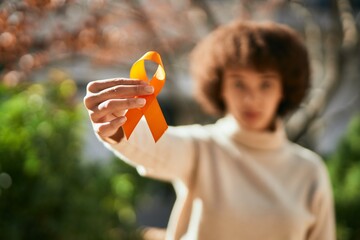 Young hispanic girl with serious expression holding orange awareness ribbon at the city.