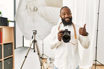 African american photographer man working at photography studio doing happy thumbs up gesture with...