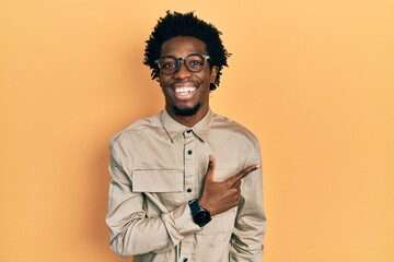 Young african american man wearing casual clothes and glasses cheerful with a smile of face pointing with hand and finger up to the side with happy and natural expression on face