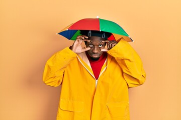 Young african american man wearing yellow raincoat trying to open eyes with fingers, sleepy and tired for morning fatigue