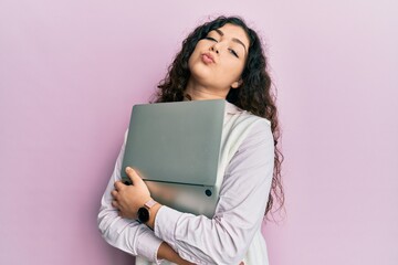 Naklejka premium Young brunette woman with curly hair hugging laptop with love looking at the camera blowing a kiss being lovely and sexy. love expression.
