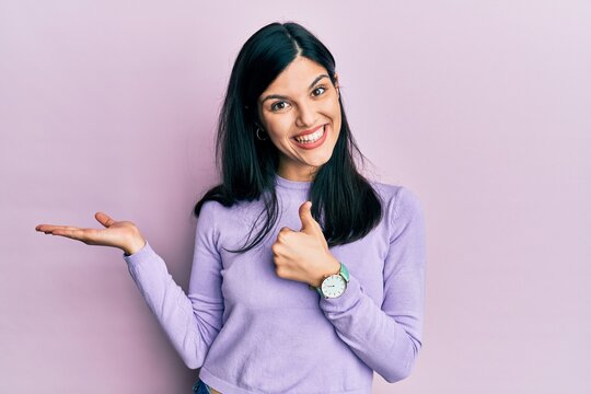 Young hispanic woman wearing casual clothes showing palm hand and doing ok gesture with thumbs up, smiling happy and cheerful