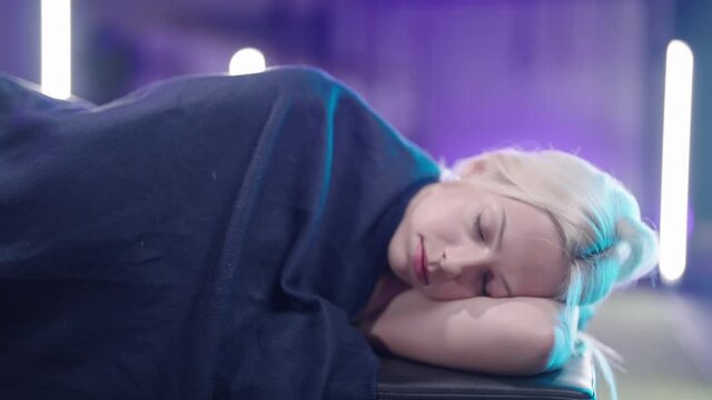 Cute blonde girl sleeping in the gym zoom out surrounded with neon lights 4K