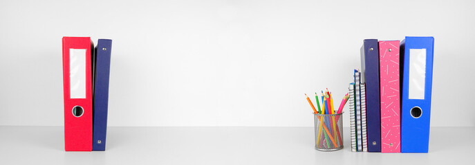 School supplies and binders on a white shelf against a white wall banner background. Back to school...