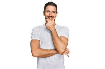 Fototapeta premium Handsome man with beard wearing casual white t shirt looking confident at the camera smiling with crossed arms and hand raised on chin. thinking positive.