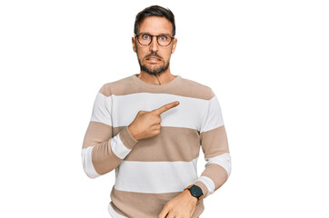 Handsome man with beard wearing casual clothes and glasses pointing aside worried and nervous with...