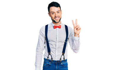 Hispanic man with beard wearing hipster look with bow tie and suspenders smiling with happy face...