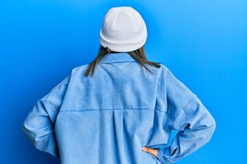 Young latin woman wearing cute wool cap standing backwards looking away with arms on body