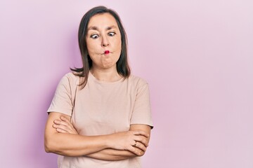 Fototapeta premium Middle age hispanic woman with arms crossed gesture making fish face with mouth and squinting eyes, crazy and comical.