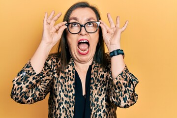 Middle age hispanic woman wearing business clothes and holding glasses angry and mad screaming frustrated and furious, shouting with anger looking up.
