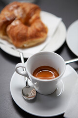 Traditional Italian breakfast. Fresh croissants with cream and sugar powder, espresso coffee and cappuccino on a black wooden table in Milan, Lombardy, Italy. European food and pastry.