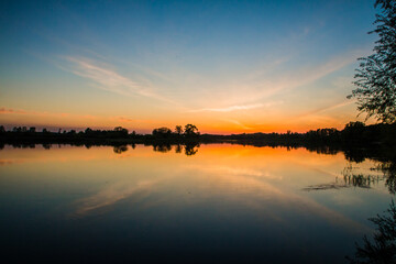 Orange sunset in the bright blue sky over the lake