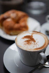 Traditional Italian breakfast. Fresh croissants with cream and sugar powder, espresso coffee and cappuccino on a black wooden table in Milan, Lombardy, Italy. European food and pastry.