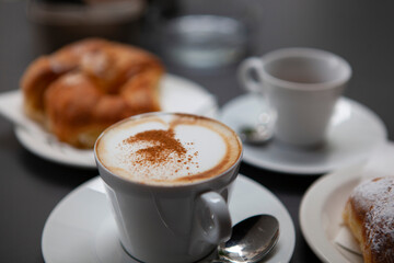 Traditional Italian breakfast. Fresh croissants with cream and sugar powder, espresso coffee and cappuccino on a black wooden table in Milan, Lombardy, Italy. European food and pastry.