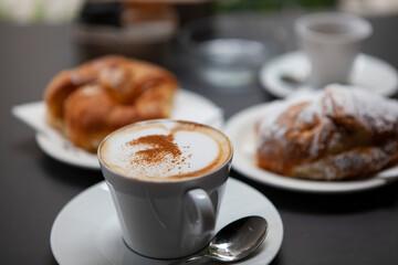 Traditional Italian breakfast. Fresh croissants with cream and sugar powder, espresso coffee and cappuccino on a black wooden table in Milan, Lombardy, Italy. European food and pastry.
