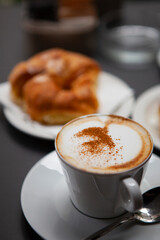 Traditional Italian breakfast. Fresh croissants with cream and sugar powder, espresso coffee and cappuccino on a black wooden table in Milan, Lombardy, Italy. European food and pastry.