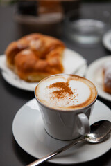 Traditional Italian breakfast. Fresh croissants with cream and sugar powder, espresso coffee and cappuccino on a black wooden table in Milan, Lombardy, Italy. European food and pastry.