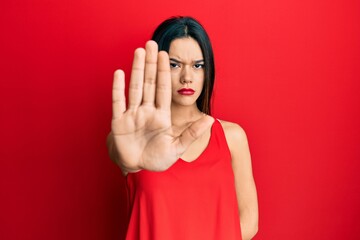 Young hispanic girl wearing casual style with sleeveless shirt doing stop sing with palm of the hand. warning expression with negative and serious gesture on the face.