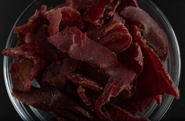 Jerky beef, jerky in a glass bowl on a dark background. Rustic country style dried meat. Delicious meat snack.