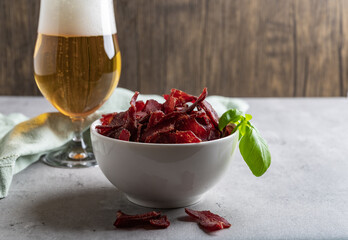Jerky Beef, Jerky in white bowls with fresh basil on a concrete-wood background. Delicious dried meat snack with pilsner in rustic country style.