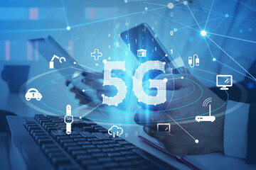 Office workplace with two colleagues who are working with digital devices including smartphone. Blue hologram icons of 5G digital network. Wireless systems and high speed signal