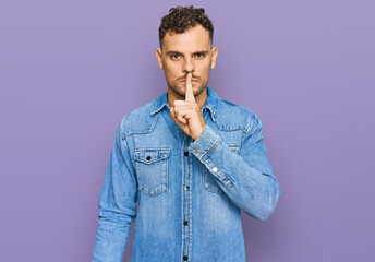 Obraz premium Young hispanic man wearing casual denim jacket asking to be quiet with finger on lips. silence and secret concept.