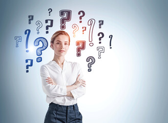 European attractive business woman with crossed arms pose looking at camera and pondering about career opportunities. Question marks drawn on light blue wall behind. Concept of searching for an answer