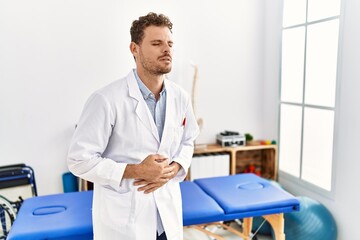 Fototapeta premium Handsome young man working at pain recovery clinic with hand on stomach because indigestion, painful illness feeling unwell. ache concept.
