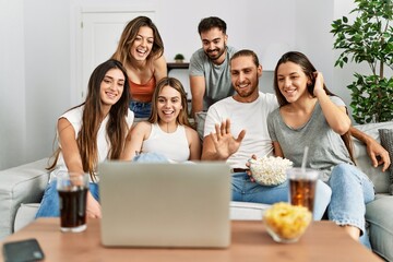 Group of young friends having video call using laptop sitting on the sofa at home.