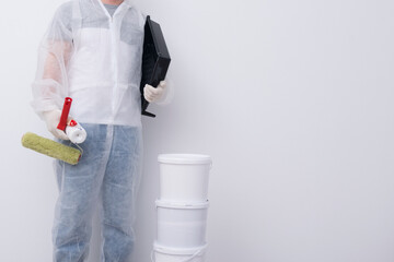 a man in protective clothing, with paint rollers in his hands, put three buckets on top of each other, against the background of a white wall, there is a place for the inscription © kurgu128