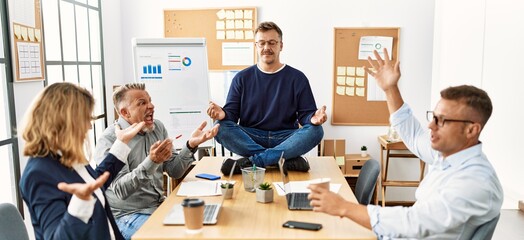 Businessman enjoys meditating during meeting. Sitting on desk near arguing partners at the office.