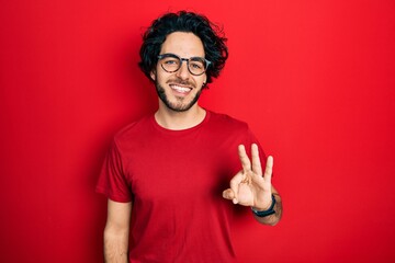 Handsome hispanic man wearing casual t shirt and glasses showing and pointing up with fingers number three while smiling confident and happy.