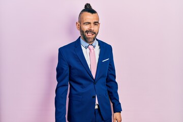 Young hispanic man wearing business suit and tie winking looking at the camera with sexy...