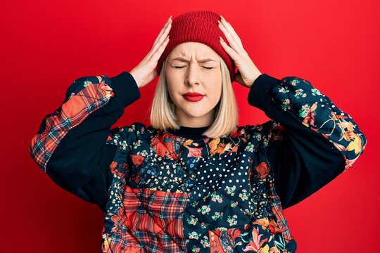 Young blonde woman wearing wool winter cap suffering from headache desperate and stressed because pain and migraine. hands on head.