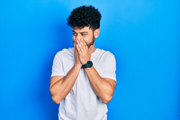 Fototapeta na wymiar Young arab man with beard wearing casual white t shirt laughing nervous and excited with hands on chin looking to the side