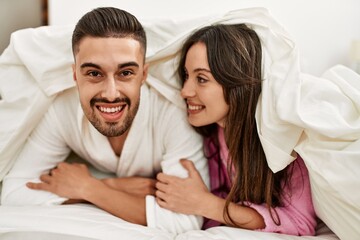Young hispanic couple smiling happy lying in bed at home.