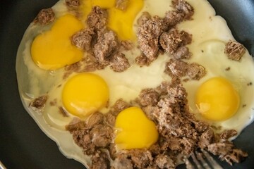 fried eggs and ground beef in a frying pan on an oven