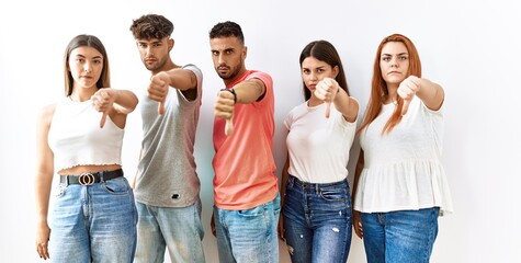 Group of young friends standing together over isolated background looking unhappy and angry showing rejection and negative with thumbs down gesture. bad expression.