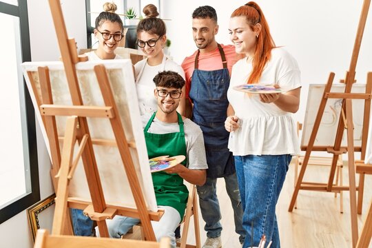 Group of young paint students smiling happy and looking draw of partner at art studio.
