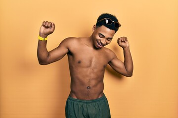 Young african american man wearing swimwear and swimmer glasses dancing happy and cheerful, smiling moving casual and confident listening to music